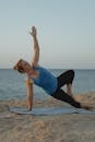 Woman in Blue Tank Top and Black Leggings Doing Yoga on Beach